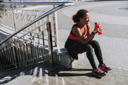 Joyful Afro American girl holding bottle of water