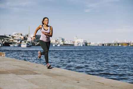 Smiling Afro American lady running along the riverの写真素材