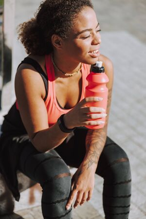 Charming Afro American lady holding bottle of water