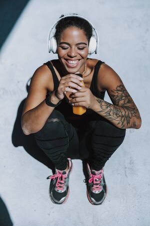 Cheerful young woman in headphones holding bottle of juice