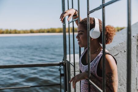 Beautiful Afro American lady in headphones looking at the riverの写真素材