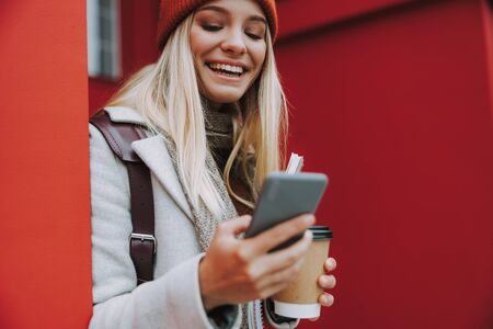 Young woman with coffee using smartphone and smiling wide