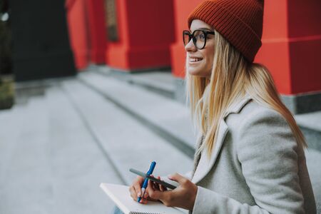 Happy lady with smartphone writing in copybookの写真素材