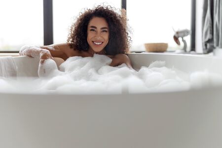 Cheerful Afro American lady taking bath at homeの写真素材