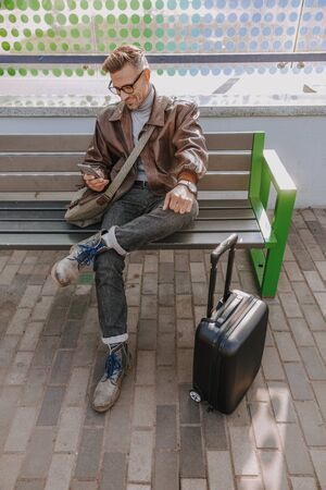 Handsome smiling man sitting on bench and using cellphoneの写真素材