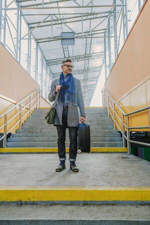 Elegant young man holding travel suitcase and smiling