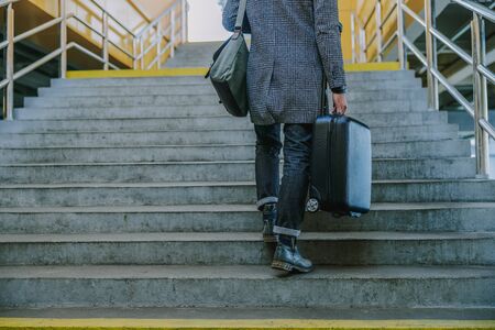 Young man with trolley bag walking up the stairsの写真素材