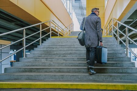 Stylish gentleman with travel suitcase walking up the stairs