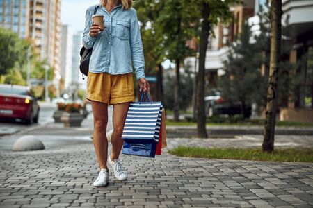 Cropped photo of a woman outdoors with a paper cup of coffee and colorful shopping bags. Website bannerの写真素材