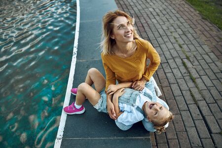 Happy woman relaxing with daughter on the fountain