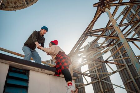 Guy helping the girl climbing on the roof