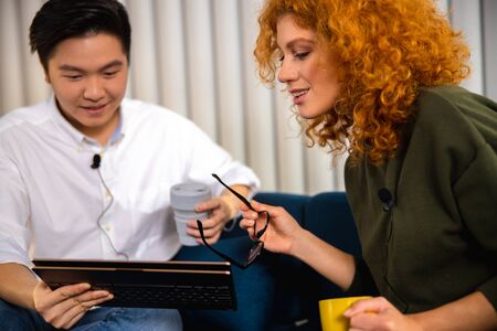 Smiling man with coffee looking at tablet with lady next to himの写真素材