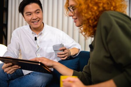 Happy Asian man with tablet looking at pretty lady in office