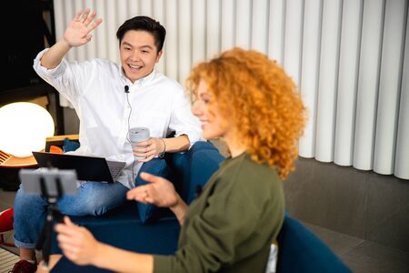 Smiling Asian man is waving hand at camera