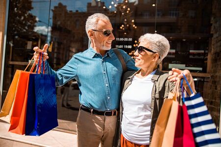 Cheerful senior couple with purchases standing on the streetの写真素材