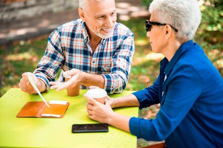 Cheerful senior man chatting with lady in outdoor cafeの写真素材