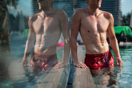 Smiling sexy man standing at the edge of the poolの写真素材