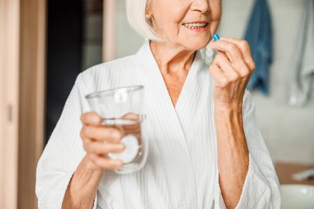 Smiling elderly woman in bathrobe taking pillsの写真素材
