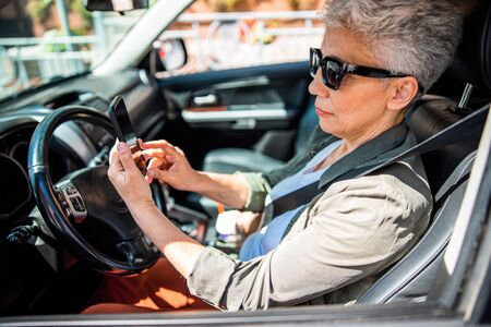 Senior lady sitting in car and using cellphoneの写真素材