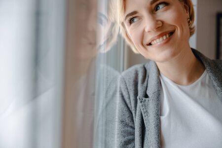 Smiling attractive woman is standing near windowの写真素材