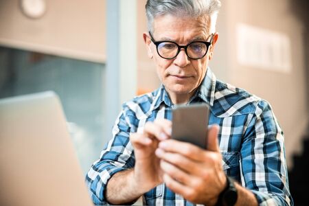 Mature man in glasses holding mobile phone in handsの写真素材