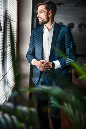 Handsome smiling stylish Caucasian entrepreneur standing indoors