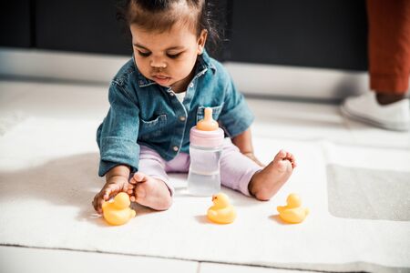 Cute Afro American baby playing with toy duck at home