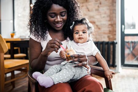 Happy loving mother spoon feeding newborn daughterの写真素材