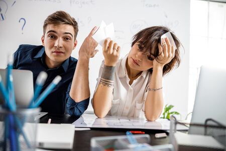 Upset young colleagues sitting at table in the office