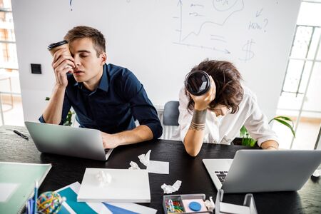 Tired young employees looking at laptops screensの写真素材