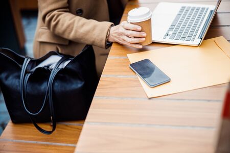 Cropped photo of a business lady with a disposable paper cup sitting at a table