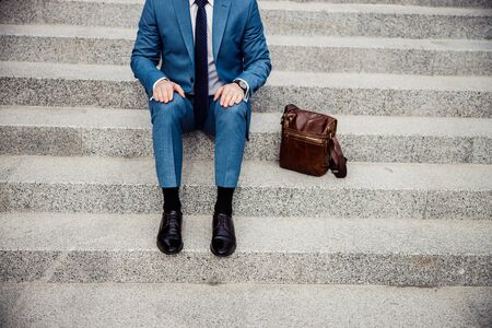 Cropped photo of a businessman with his hands on his knees sitting on the stairs