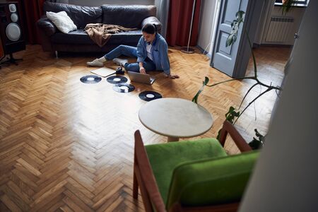 Caucasian lady in denim shirt sitting on floor among vinyl resords