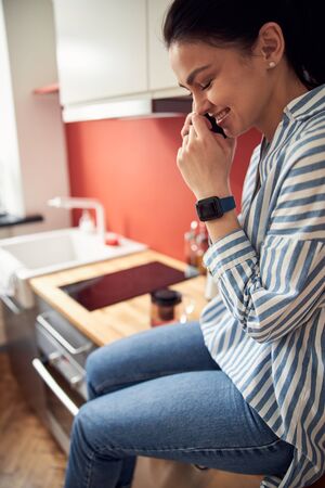 Young positive woman talking on mobile phone on cupboard indoorsの写真素材