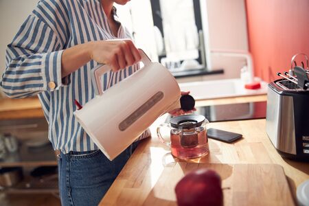 Girl pouring the hot water into teapot in the kitchen