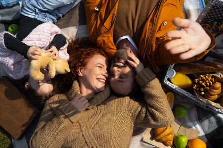 Joyful parents and their cute daughter resting during picnicの写真素材