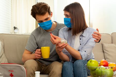 Spouses in masks sitting on couch in living room