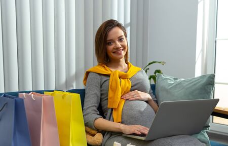 Pleased pregnant lady with presents and modern laptopの写真素材