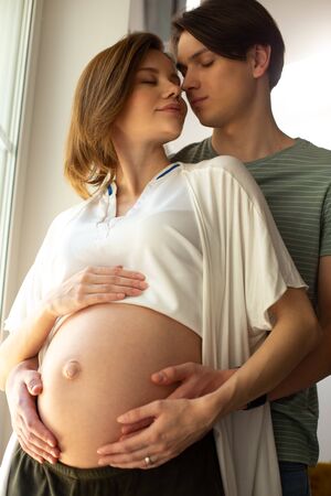 Romantic couple expecting baby standing with closed eyes