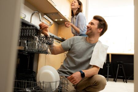 Smiling man taking dishes out of dishwasher at homeの写真素材