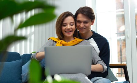 Excited young couple with modern laptop at homeの写真素材