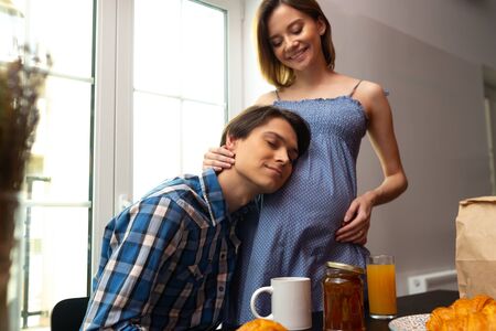 Caring man embracing pregnant woman during breakfastの写真素材