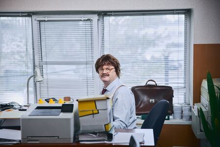 Calm male accountant in cluttered office looking curiousの写真素材