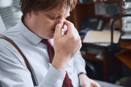 Middle-aged male office worker rubbing his nose tired of glasses