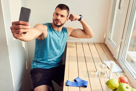 Athletic young man showing biceps muscles and making selfie
