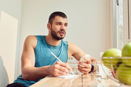 Athletic young man holding pills and making notesの写真素材
