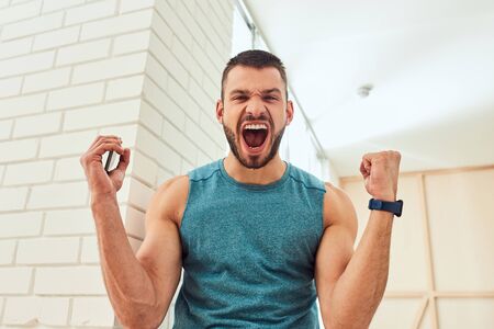 Athletic gentleman holding smartphone and screaming with joyの写真素材