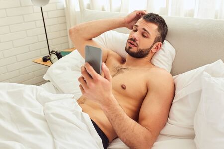 Shirtless handsome gentleman using cellphone in bedroomの写真素材