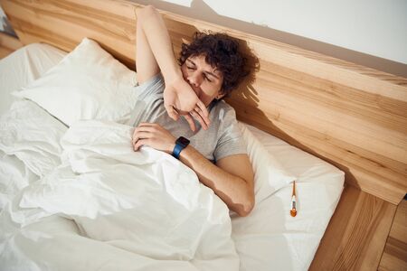 Handsome young man lying in bed and yawningの写真素材