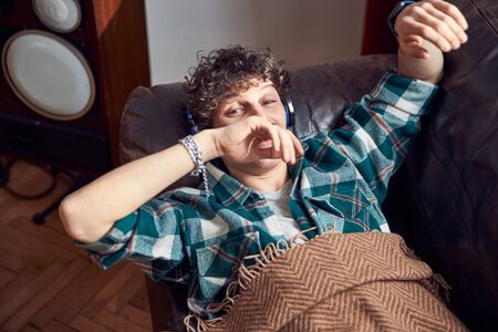 Curly-haired guy resting on couch and listening to music